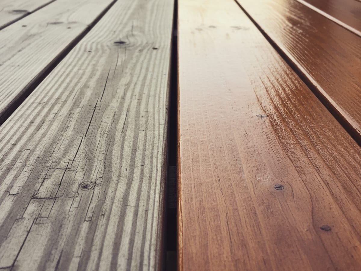 Close-up of deck boards showing weathered gray wood on the left and freshly stained boards on the right, illustrating the difference after maintenance